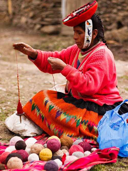 Peruvian woman is spinning the yarn with a drop-spindle