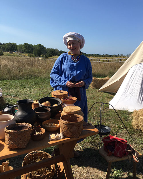 Woman in medieval attire shows reconstructed kitchen utensils