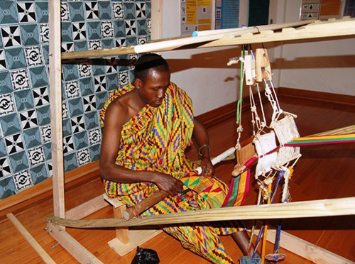 Man in kente cloth hand-weaving on wooden loom