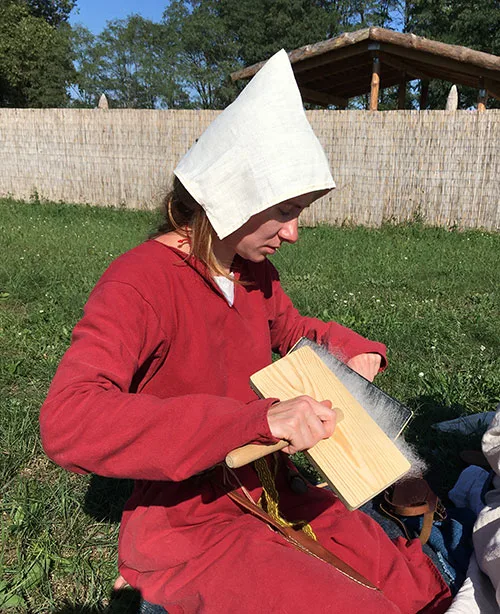 Woman dressed in medieval Irish costume carding wool fibers before spinning
